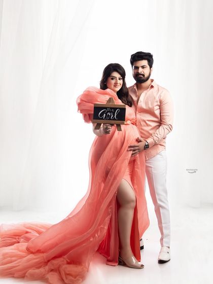 A joyful gender reveal moment within the maternity shoot. The 'It's a Girl' sign adds a personal and exciting element to this beautiful couple's portrait in a flowing pink gown.