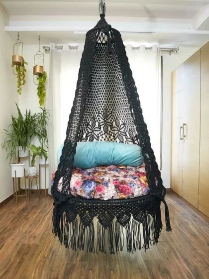 A black macrame swing with a floral cushion. The contrast between the dark macrame and the colorful cushion creates a striking and modern look.