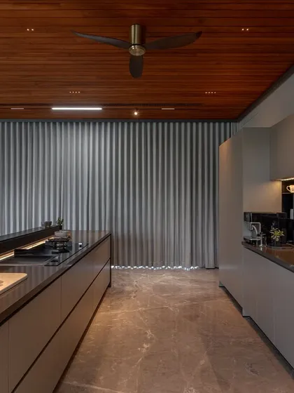 This wide view shows the kitchen's linear design, with a long island and parallel counter. The wood-paneled ceiling adds warmth and texture, balancing the cool tones of the cabinetry and floor.