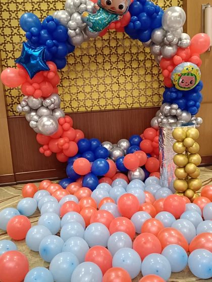 A Cocomelon themed balloon ring in red, blue, and silver. This setup is perfect for a toddler's party, with character foil balloons and a floor covered in extra balloons for a playful atmosphere.