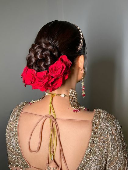 A detailed shot of the beautiful hair accessory, a classic floral bun with red roses, which adds a traditional touch to this modern gold bridal look.