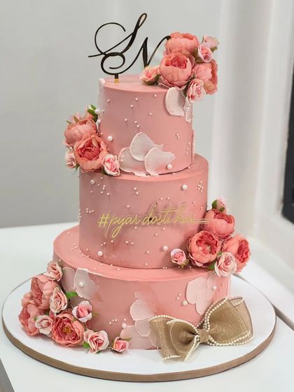 A three-tiered blush pink cake adorned with delicate florals, pearls, and a beautiful velvet bow. This design was crafted to make a special engagement day feel both grand and magical.