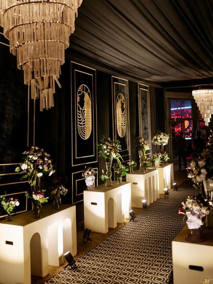 An elegant and moody Sangeet entrance, with a black and gold color scheme, Art Deco details, and dramatic tiered chandeliers.
