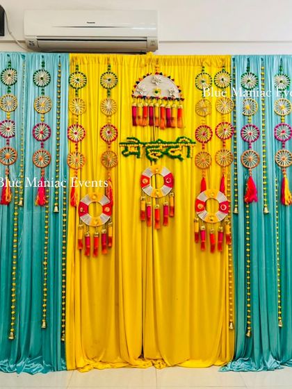 A unique Mehendi backdrop with blue and yellow drapes and a variety of traditional and bohemian-style hangings.
