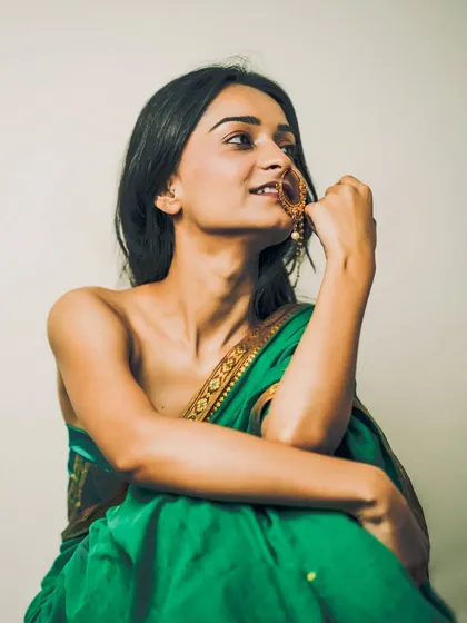 A bold and artistic portrait of a woman in a green saree, worn in a modern, strapless style, highlighting her smile and traditional nath.