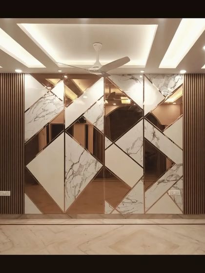 The feature wall from our pre-wedding renovation project, crafted with an intricate pattern of wood, white marble laminate, and rose-gold mirrors to create a glamorous focal point.