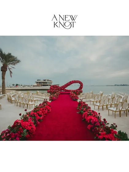 A vibrant red floral aisle leading to an infinity-symbol mandap on the beach in Doha, Qatar. This shows our capability to execute large-scale, custom-designed structures in international beach destinations.