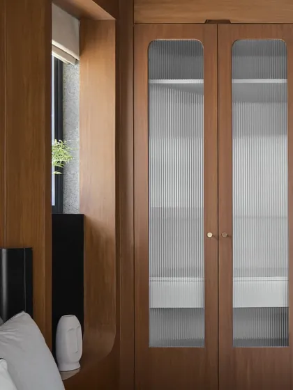 A closer view of the fluted glass wardrobe, which morphs into a wall unit that frames a window. This innovative solution is a great example of the Japandi ethos of functional, beautiful design.