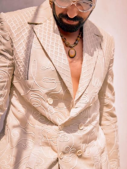 A close-up of the abstract face embroidery on our double-breasted white jacket. This unique detail proves that simplicity can still steal the show.