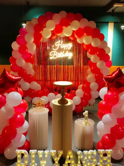 A bold red and white balloon arch with a red tinsel backdrop and a neon sign.