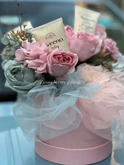 A close-up of a beautiful floral arrangement in a pink hat box, cleverly incorporating Aveeno baby lotion. It's a perfect gift that combines beauty for mom and practicality for baby.