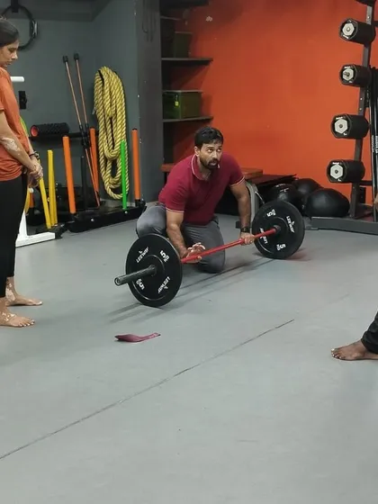 A trainer demonstrates a specific weightlifting technique from a kneeling position, showing adaptive ways to teach and perform exercises.
