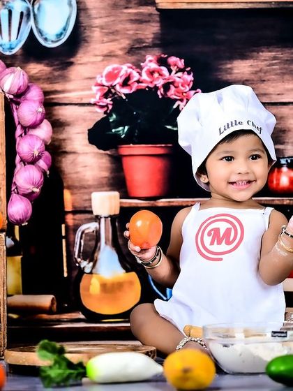 A little chef sitting amidst a colorful array of vegetables and kitchen props.
