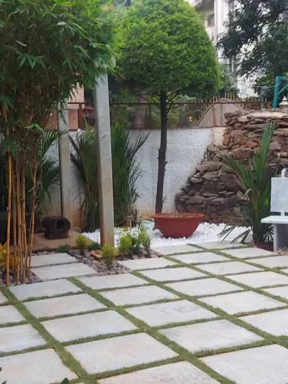 A garden seating area with a stone bench and a large paved patio. The design incorporates bamboo and topiary trees to add vertical interest and a touch of Asian-inspired design.