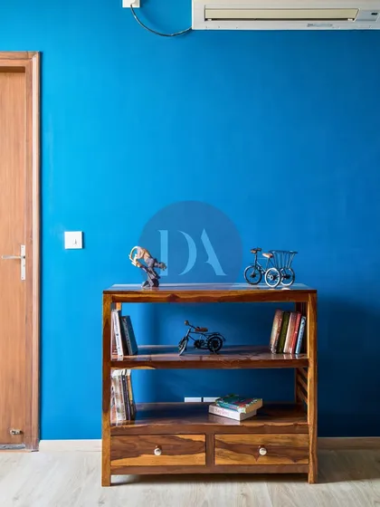 A close-up of the wooden bookshelf and decor against the blue wall. The small decorative pieces, like the miniature bicycle, add a touch of personal charm to the room.