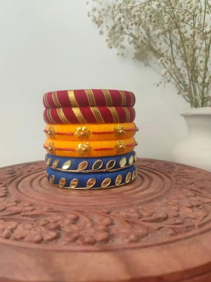 This stack of thread bangles in red, yellow, and blue is a classic festive combination. The set includes different designs, from gota patti work to mirror embellishments.