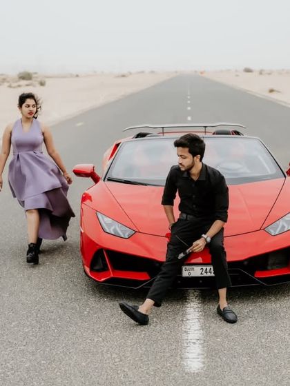 A wide shot of the couple and the Lamborghini on the desert road, capturing the vastness of the landscape.