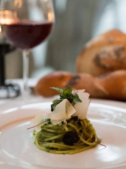 A beautiful plate of spaghetti with pesto, garnished with fresh basil and parmesan shavings. This dish is paired with a glass of red wine for a classic Mediterranean meal.