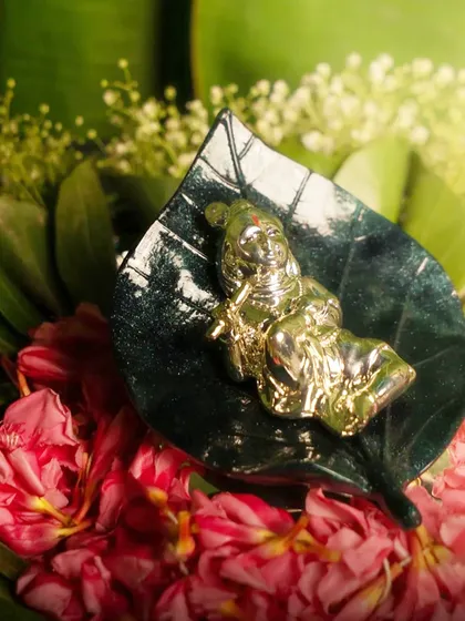 A tiny, precious idol of Bal Krishna resting on a green marble leaf. This piece is a beautiful symbol of new beginnings and divine joy, perfect for gifting on auspicious occasions.