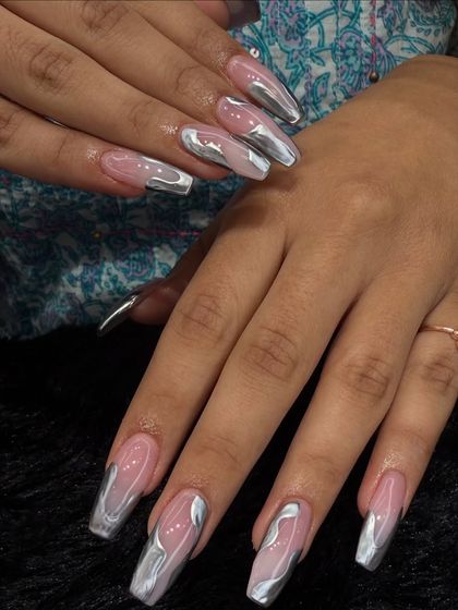 A futuristic and trendy look using silver chrome. The chrome is applied in abstract, liquid-like shapes over a sheer pink base on long, squared-off nails.