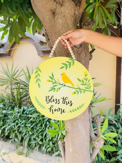 Our 'Bless This Home' wooden sign, featuring a hand-painted yellow bird. This 12-inch round sign is a beautiful and thoughtful piece to hang at your entrance, bringing blessings and charm to your home.
