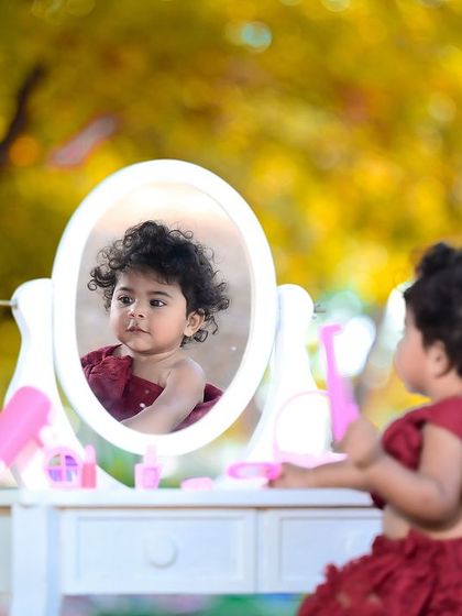 A little girl playing with makeup props in a beautiful outdoor setting, looking at her reflection in the mirror.
