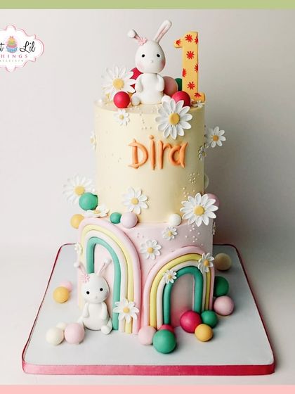 A whimsical first birthday cake featuring rainbows, daisies, and cute bunnies. This two-tiered pastel creation is a dream come true for a sweet celebration.