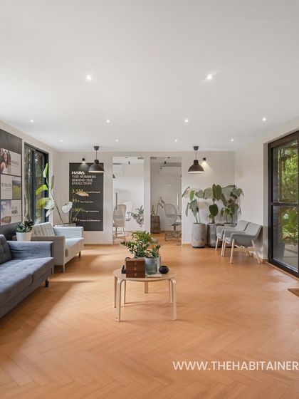 The spacious interior of a site office made from shipping containers, featuring herringbone wood flooring and large glass doors.