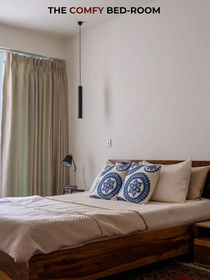 This comfy bedroom is the perfect spot to relax. The solid wood bed, patterned cushions, and minimalist lighting create a tranquil and inviting atmosphere.