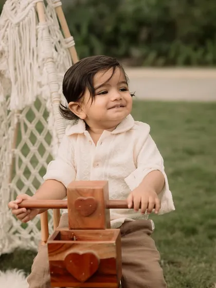 A candid smile from this little one as he plays with a wooden tricycle in the park.