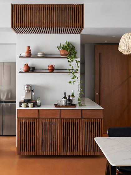 This bar and coffee station features custom cabinetry with vertical wood slats. The design conceals storage while adding a strong rhythmic pattern to the kitchen and dining area.