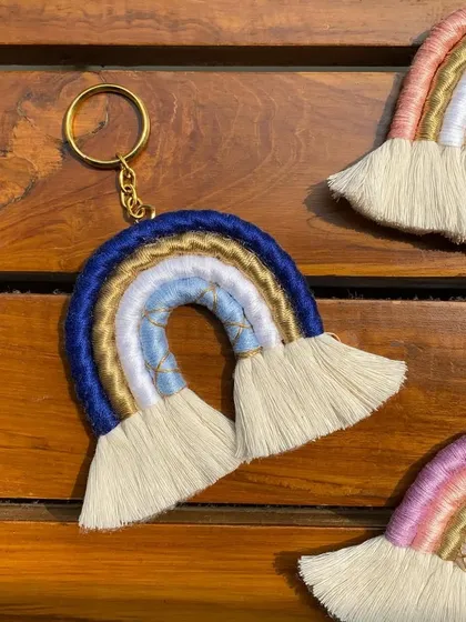 A detailed shot of the blue, white, and gold macrame rainbow keychain. The intricate wrapping and fluffy tassels make this a sturdy and stylish handmade charm.
