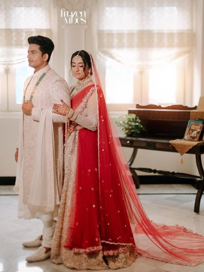 A formal portrait with a touch of vintage elegance. The bride's red veil adds a beautiful pop of color against their coordinated outfits.