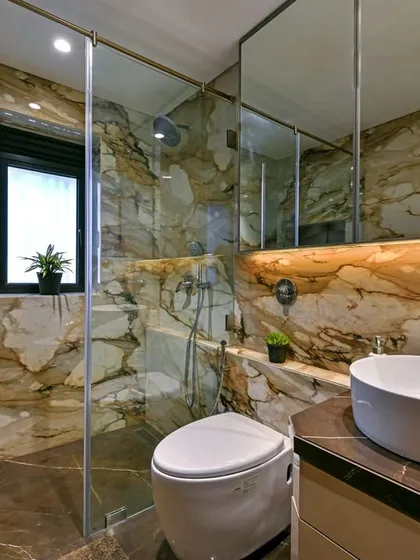 We used a warm, golden-toned marble to envelop this bathroom, creating a rich and inviting atmosphere. The modern vessel sink and glass shower partition maintain a clean and contemporary feel.