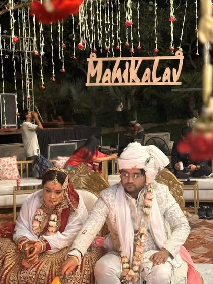 A candid moment from a wedding, with the couple seated against a backdrop of hanging floral strings and a custom wooden hashtag sign.
