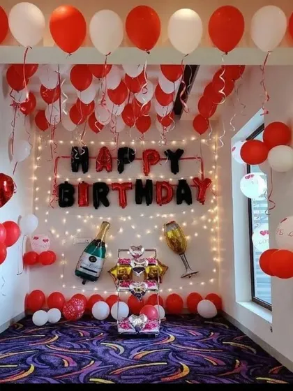 A dedicated party room setup for a birthday celebration. This design uses red and white balloons, 'Happy Birthday' foil letters, and champagne-themed foil balloons to create a fun photo corner.
