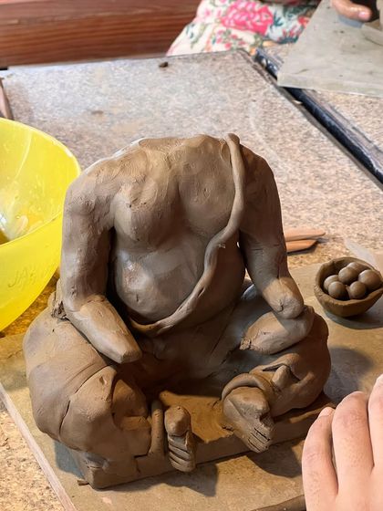 The beginning stages of a Ganesha idol, with the torso formed and a bowl of modaks ready to be placed.