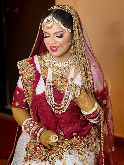 A beautiful Gujarati bride adorned in a layered Polki and Kundan set, featuring a long rani haar. The red and white panetar saree is perfectly complemented by the heavy jewellery.