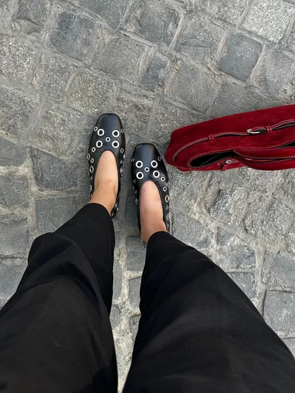 A street-style view of the black eyelet ballet flats paired with a red suede bag. This is how I love to see my pieces worn, as part of a real-life look that is both stylish and practical.