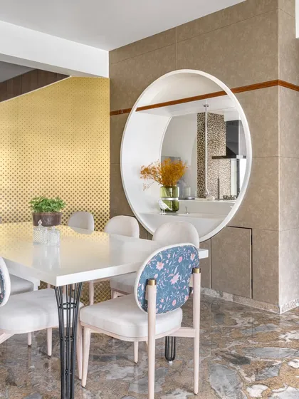 A whimsical touch in this Mumbai apartment, where a circular partition with a hidden Corian wash basin separates the dining area. The floral-patterned chair and bold gold backdrop add a layer of playful sophistication.