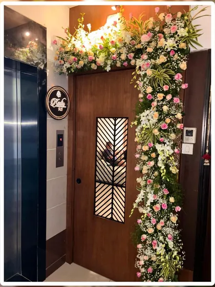 An elegant and asymmetrical floral design for a modern apartment door. This arrangement uses soft pink and white roses with baby's breath, gracefully cascading down one side of the entrance.