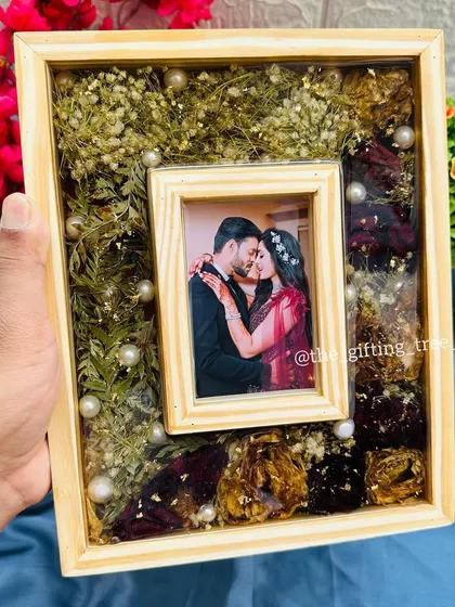 The pinewood frame held in hand, giving a clear view of the central photo and the surrounding floral arrangement.