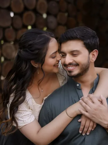An intimate embrace against a rustic, wooden background. This shot captures the couple's easy chemistry, with their coordinated casual wear reflecting a comfortable and authentic style.