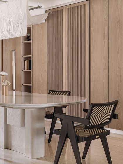 A detail of the dining area, where a monolithic white marble table takes center stage. The surrounding custom cabinetry in natural wood veneer provides ample storage while maintaining the home's clean, uncluttered aesthetic. Every element is chosen for its form and function.