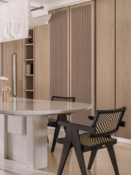 The dining area features a monolithic white marble table we designed, surrounded by elegant chairs. The fabric light fixture above adds a soft, diffused glow to the space.