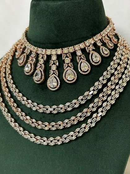 A layered necklace set combining a rose-gold plated AD choker with simpler chains. This rental set is perfect for a contemporary look.