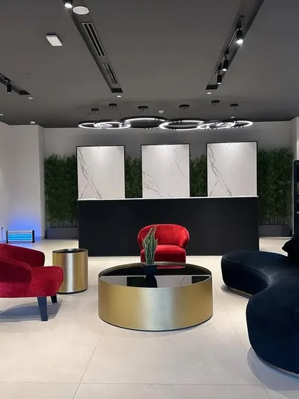 This is the waiting lounge at the ALP Overseas Experience Center in Kota. The design combines bold furniture choices like the red and black velvet chairs with a sleek, minimalist reception desk and modern ring lighting to create a luxurious and contemporary feel.