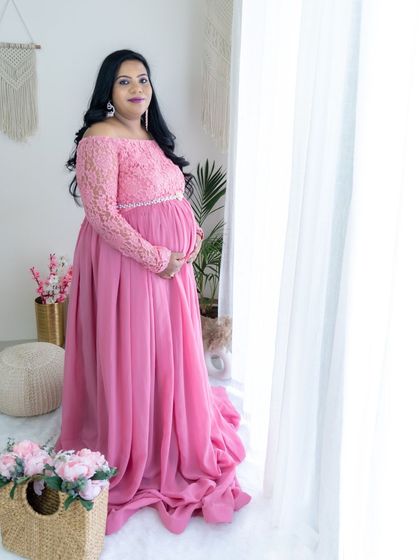 A beautiful studio portrait by the window. The mom-to-be looks elegant in a pink lace-top gown.