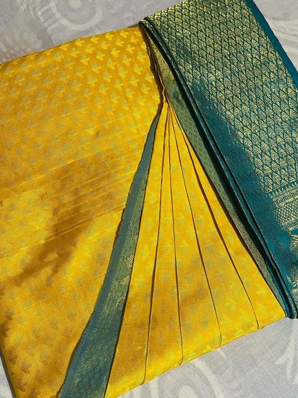 A bright yellow Kanjivaram saree with a contrasting teal border. The pleats are done so the beautiful border is highlighted.