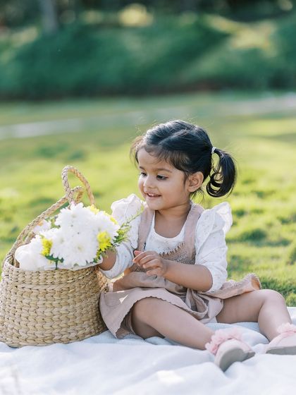 A little girl sitting on a picnic blanket with a basket of flowers. A sweet and charming portrait.